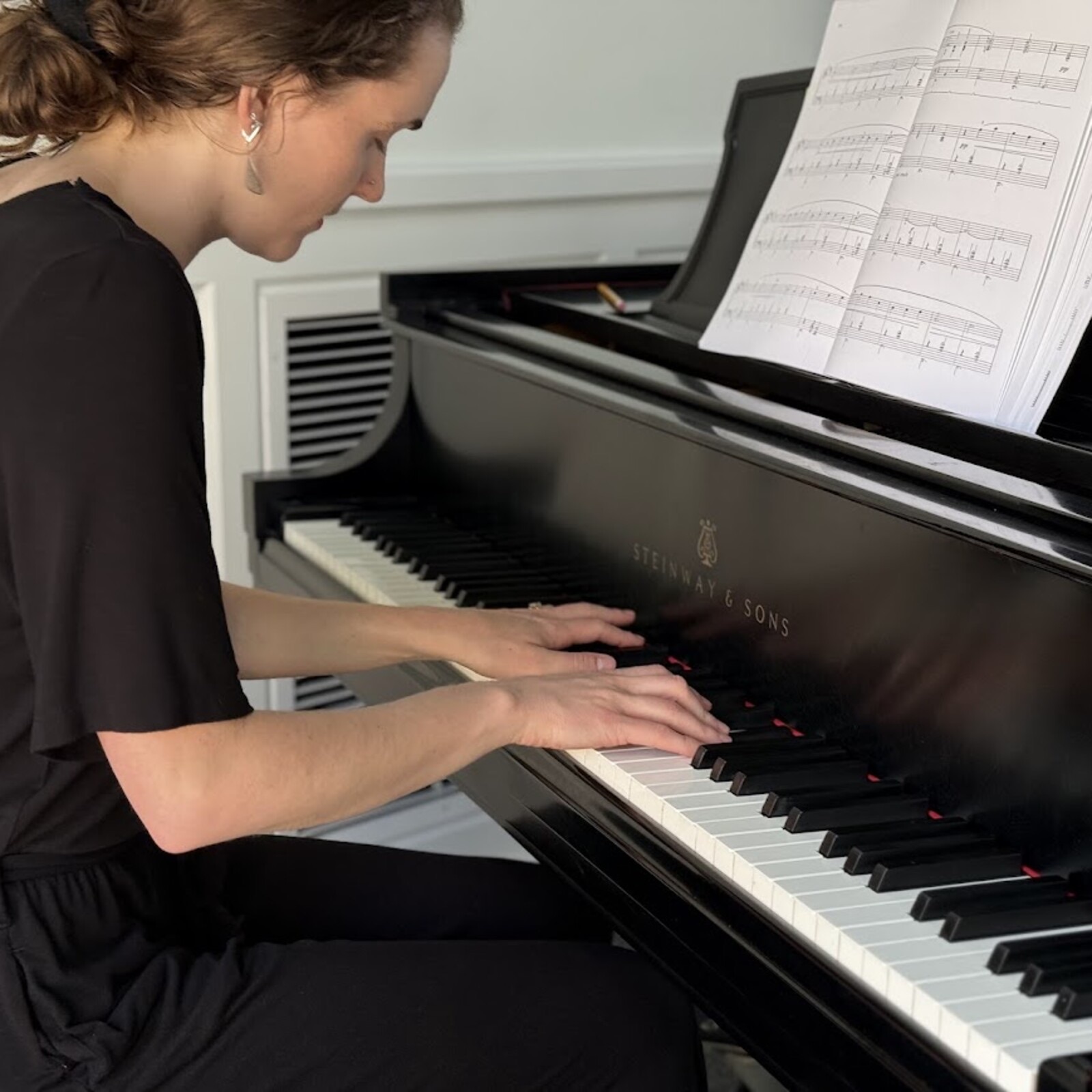 Julia Carbonneau playing classical music at a black Steinway & Sons grand piano with sheet music in front of her